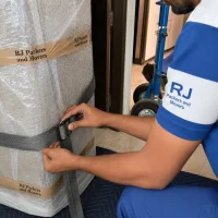 RJ Packers and Movers close-up of a professional mover fastening a heavy-duty lifting strap around a bubble-wrapped appliance