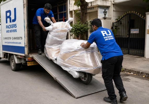 RJ Packers and Movers scooter fully protected with foam and stretch film being rolled onto a small vehicle transport ramp by RJ Packers and Movers staff