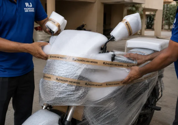RJ Packers and Movers close-up of movers protecting a motorcycle fuel tank and mirrors with foam, bubble wrap, and stretch film before transport
